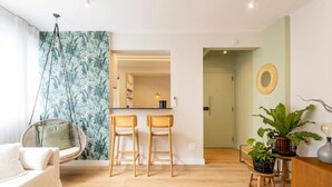Ein modernes Wohnzimmer mit einem Hängekorbsessel, zwei Barhocker, einer Couch, einem Holztisch und einem Blumentopf.