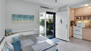 A modern kitchen with white cabinets, a microwave, and a stove. There is a dining area with a table and chairs, and a large window with blinds. - Less than 1/2 mile to beach. Community pool. (St. Simons Island)