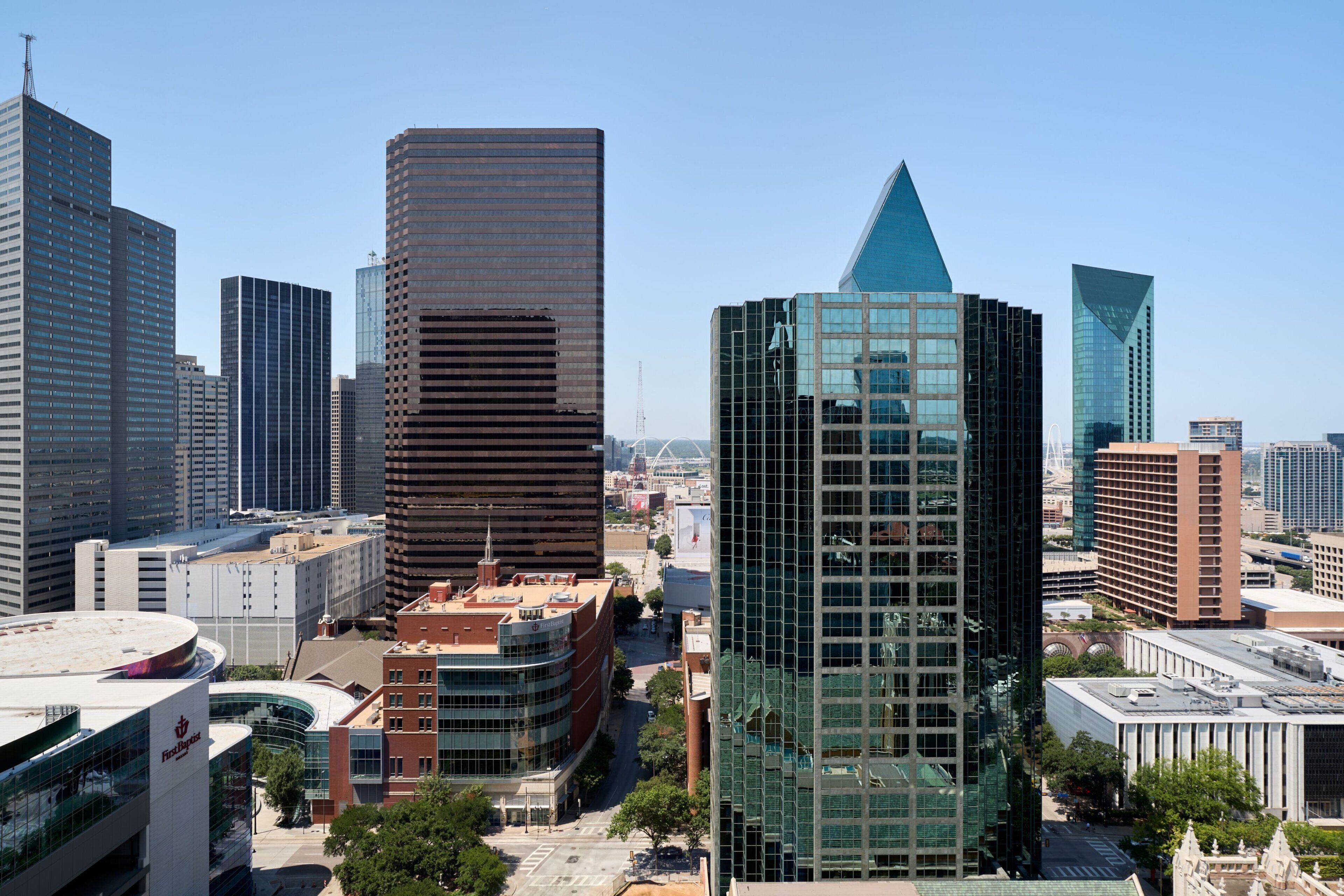 A cityscape with modern high-rise buildings, a curved building with a circular roof, and a prominent glass skyscraper.