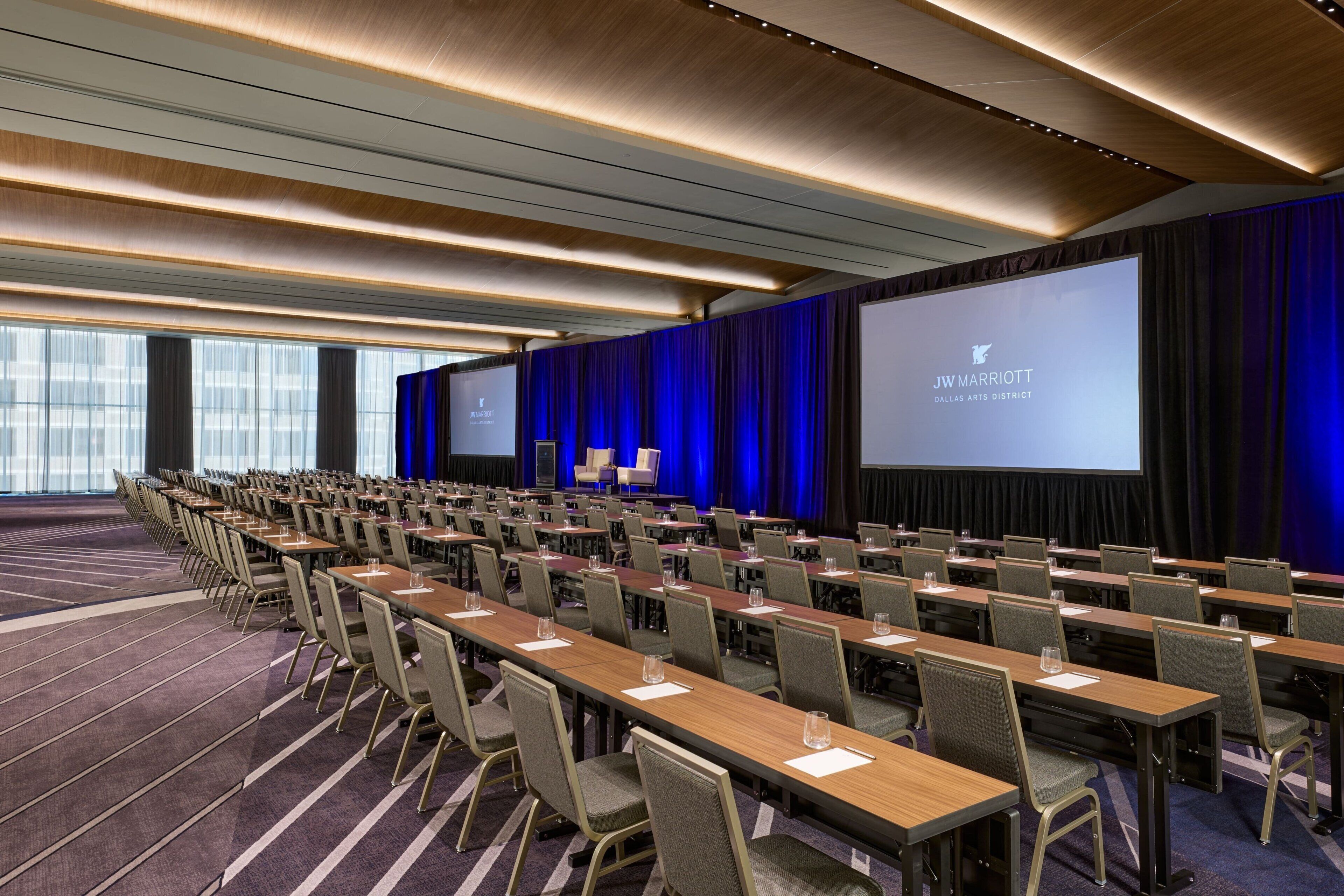 A conference room with rows of tables and chairs, a large screen, and a blue curtain backdrop.