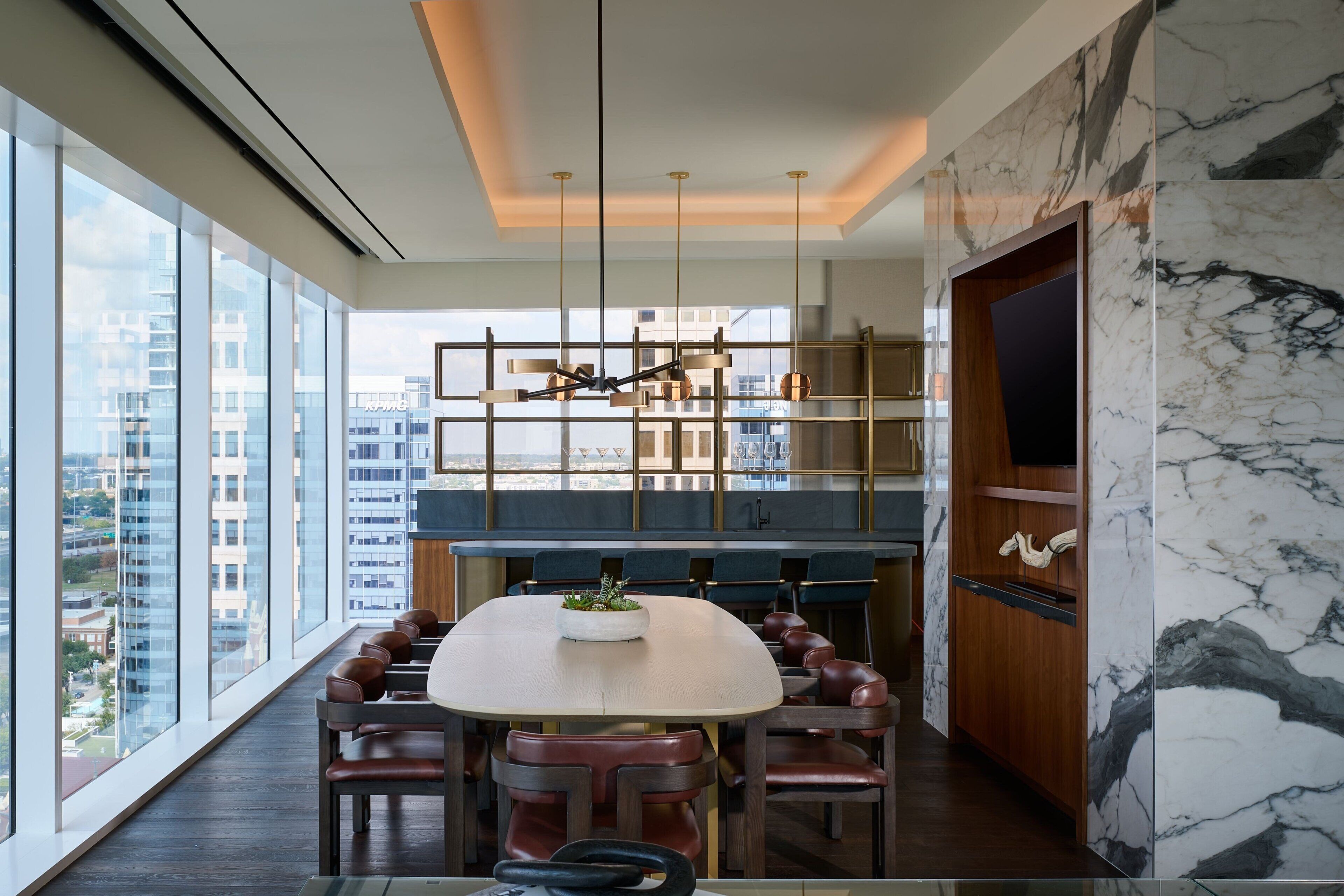 A modern kitchen with a marble backsplash, a dining area with leather chairs, and a city view through large windows.