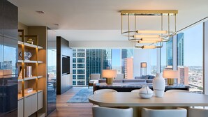A modern living room with a dining area, large windows with a city view, and a built-in bookshelf. - JW Marriott Dallas Arts District Hotel (Dallas)