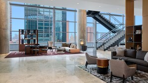 A spacious lobby with a high ceiling, large windows offering a city view, a staircase, and a seating area with a coffee table. - JW Marriott Dallas Arts District Hotel (Dallas)