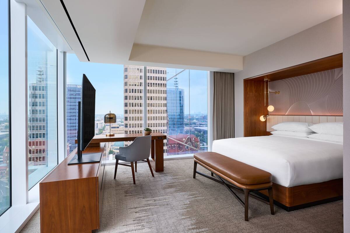 Camera d'hotel moderna con un letto grande, una scrivania con sedia, una televisione e vista sulla città attraverso ampie finestre.