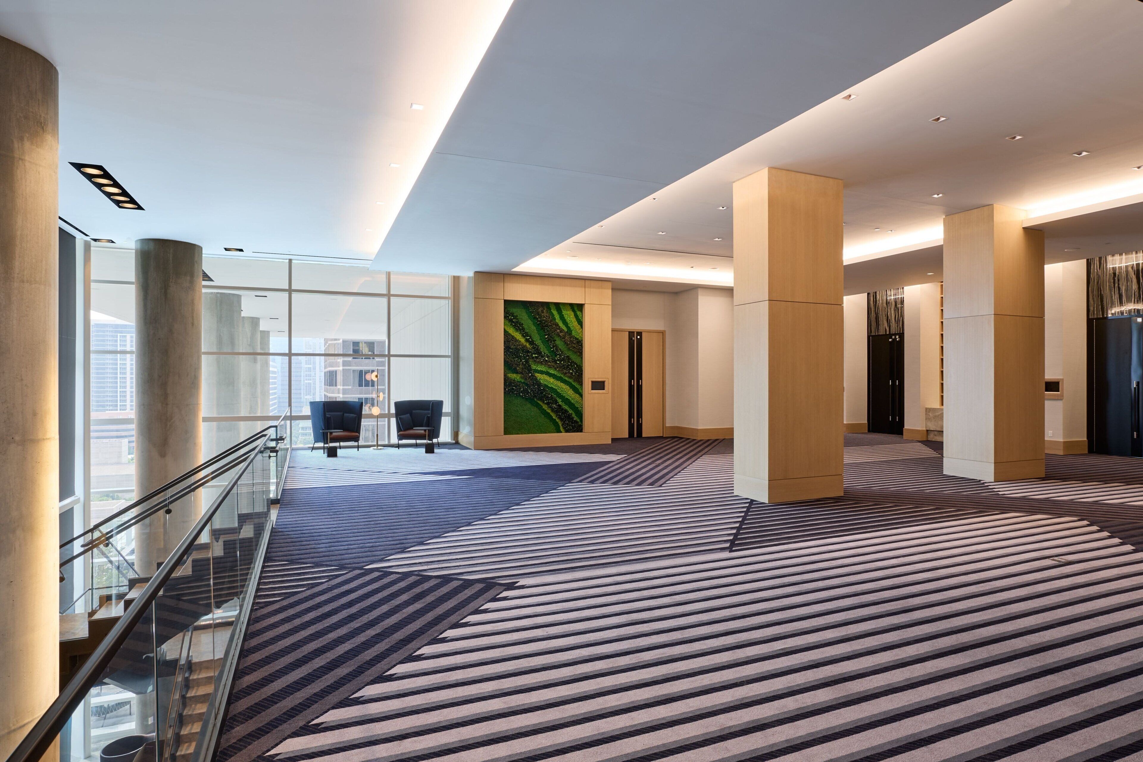 A modern hotel lobby with a glass staircase, a large abstract painting, and a patterned carpet.