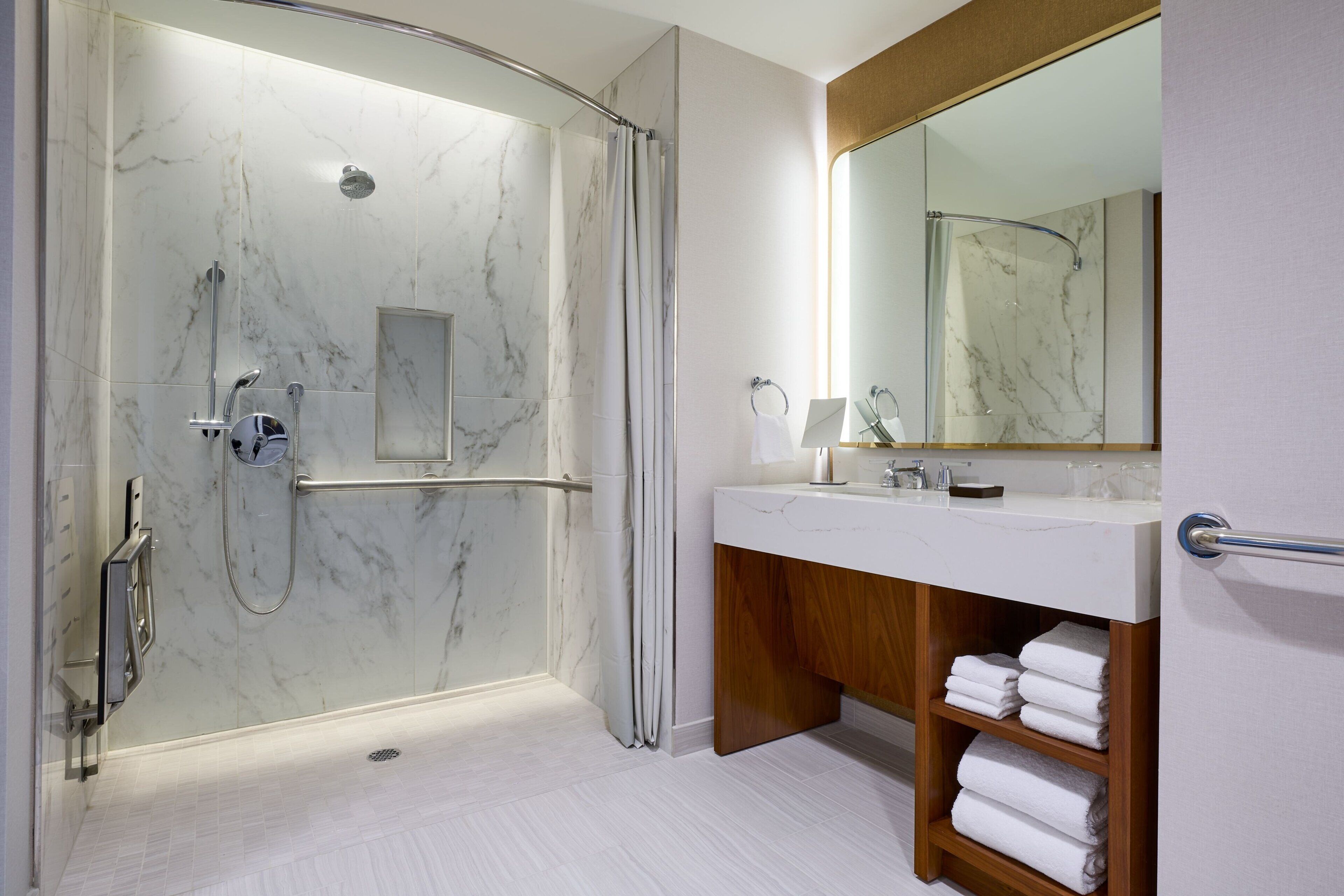 A modern bathroom with a glass-enclosed shower, a vanity with a mirror, and a wooden vanity with towels.