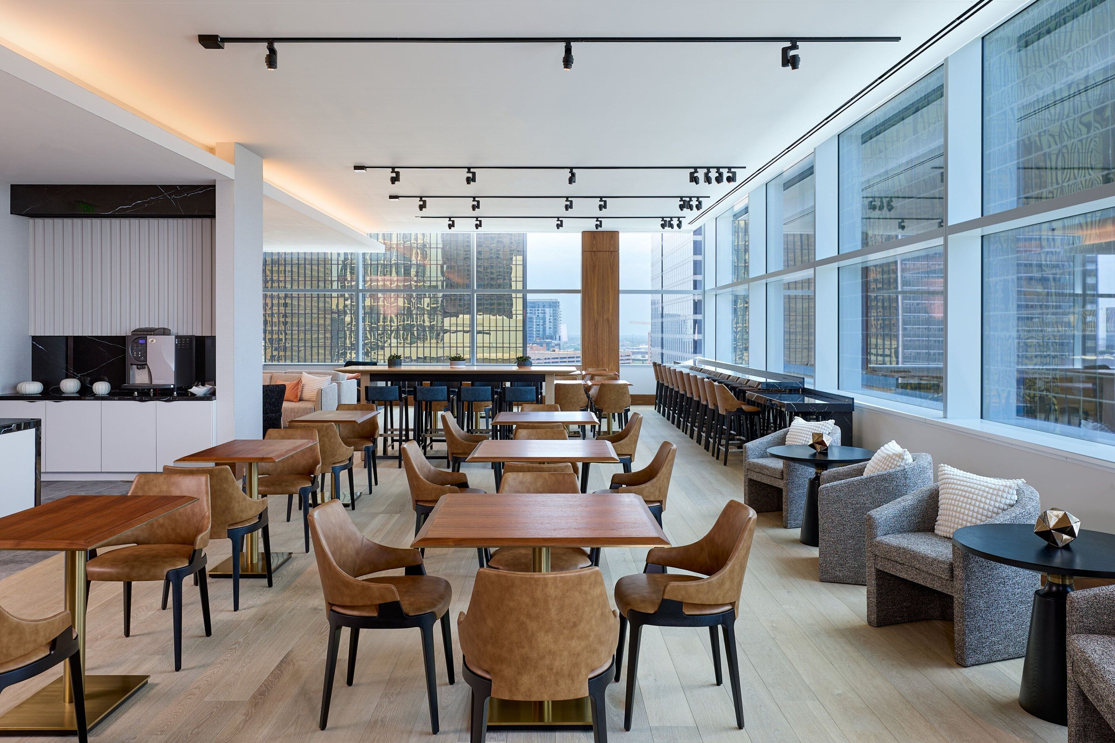 Een modern restaurant met hoge plafonds, grote ramen en diverse zitmogelijkheden, zoals tafels en banken.