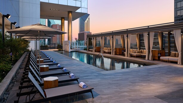 A rooftop pool area with lounge chairs and umbrellas, a pool, and a modern building in the background. - JW Marriott Dallas Arts District Hotel (Dallas)