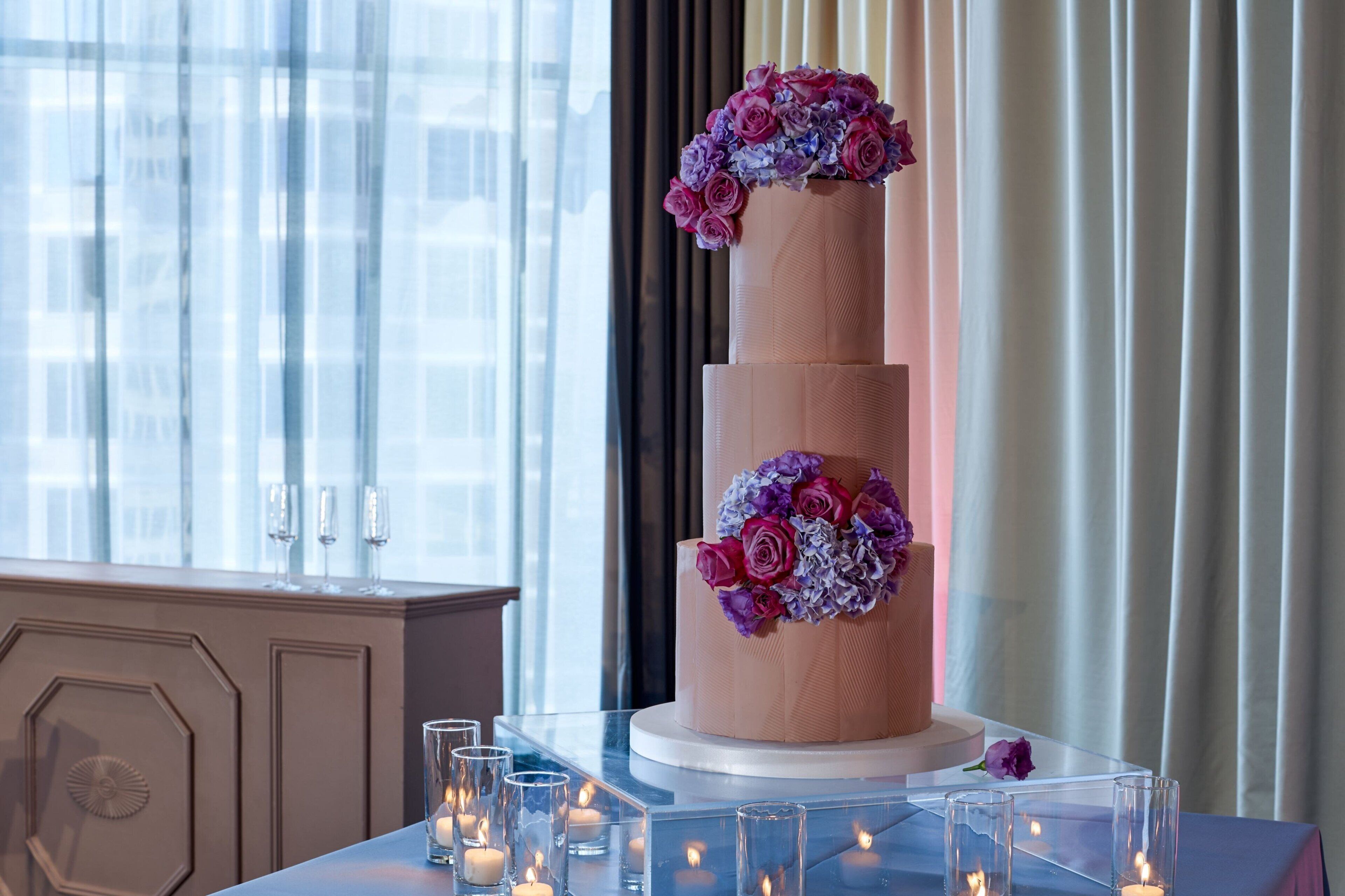 A multi-tiered cake with floral decorations on a table, surrounded by candles.