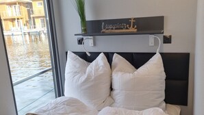 Ein Hotelzimmer mit einem Bett, weißen Kissen, einer braunen Decke, einer kleinen Pflanze auf einem Regal und Blick auf ein Gebäude durch ein Fenster.