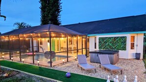Ein moderner Poolbereich im Freien mit Glasveranda, Liegestühlen und einem Whirlpool.