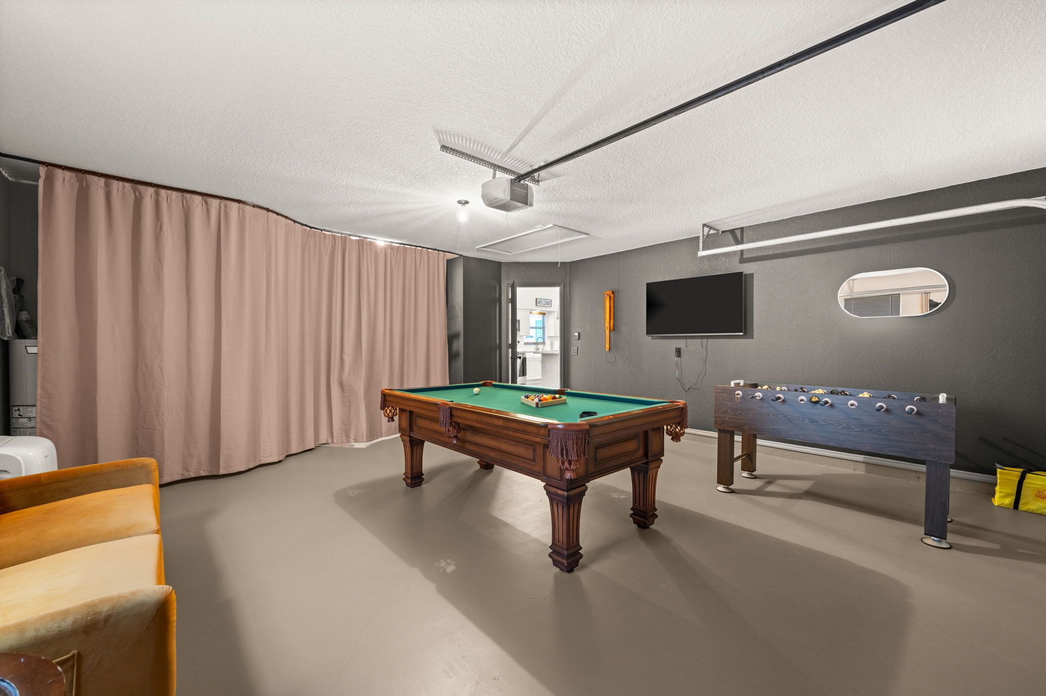 A room with a pool table, a foosball table, a television, and a large window.