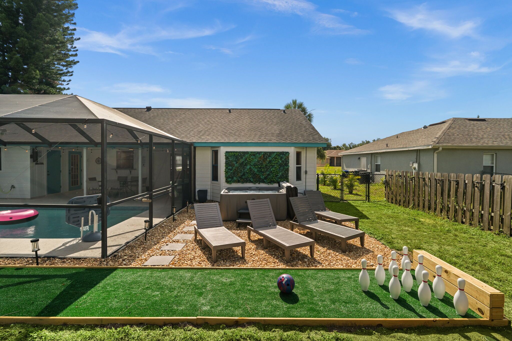 Un jardin avec une piscine, des chaises longues, un jacuzzi et une piste de bowling.