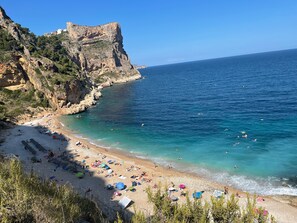 A coastal beach with rocky cliffs, clear blue sea, and umbrellas. - Modern apartment with amazing mountain views, 3 large pools, 3 bedrooms 2 baths (Benitachell)