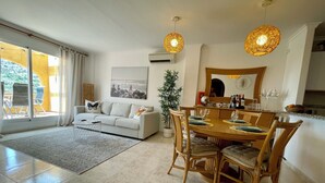 Una sala moderna con comedor, que incluye un sofá, una mesa de comedor para cuatro personas y un ventanal con cortinas.