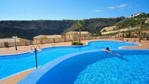 Una gran piscina exterior de diseño curvo, rodeada de edificios y un paisaje montañoso.