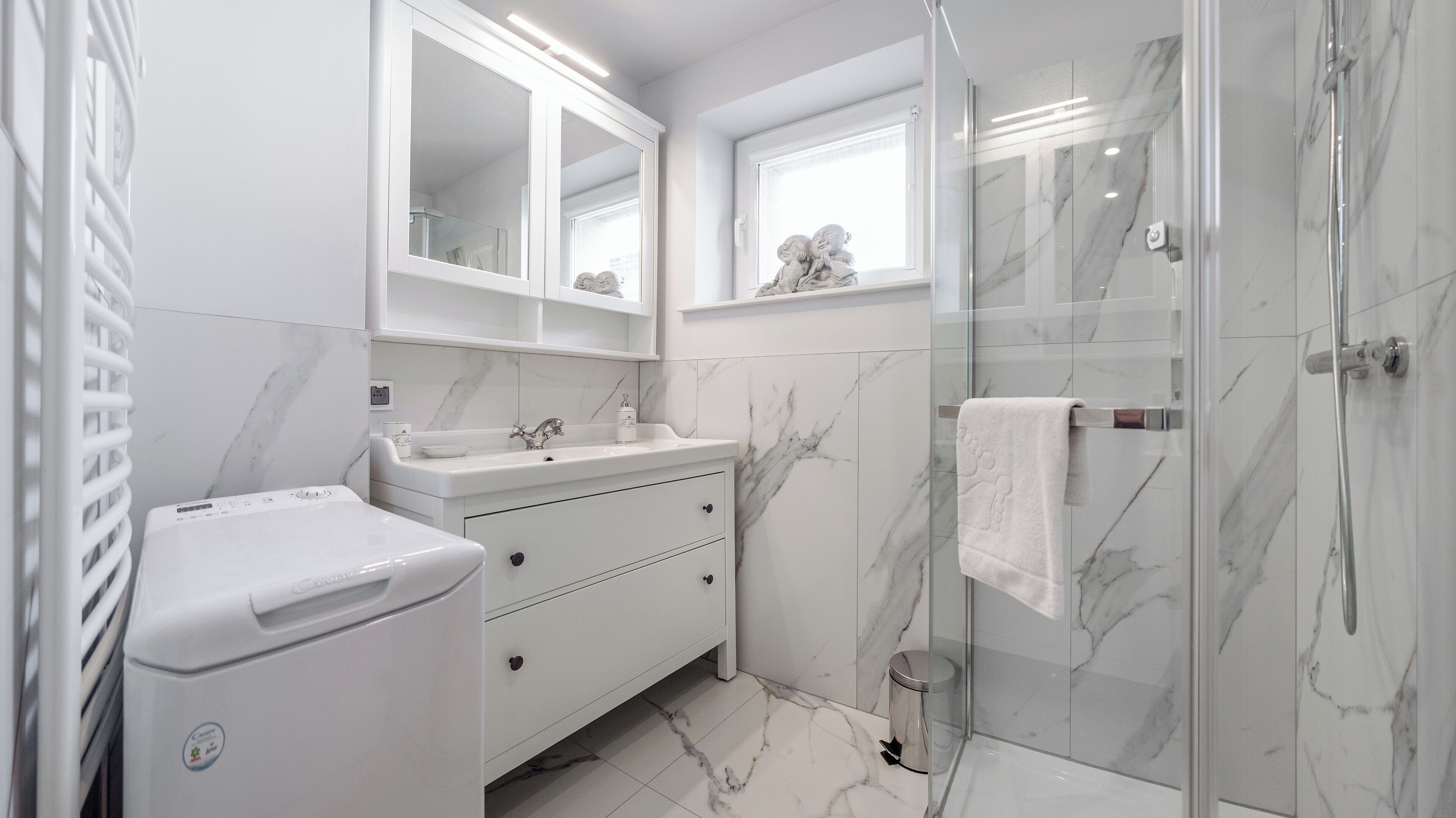 Un baño moderno con cabina de ducha de vidrio, un lavabo blanco con encimera de mármol y un espejo grande sobre el mueble.