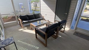Eine sonnige Terrasse mit einer Couch, zwei Stühlen und einem kleinen Tisch.