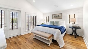A bedroom with a large bed, wooden flooring, white walls, and a bench.