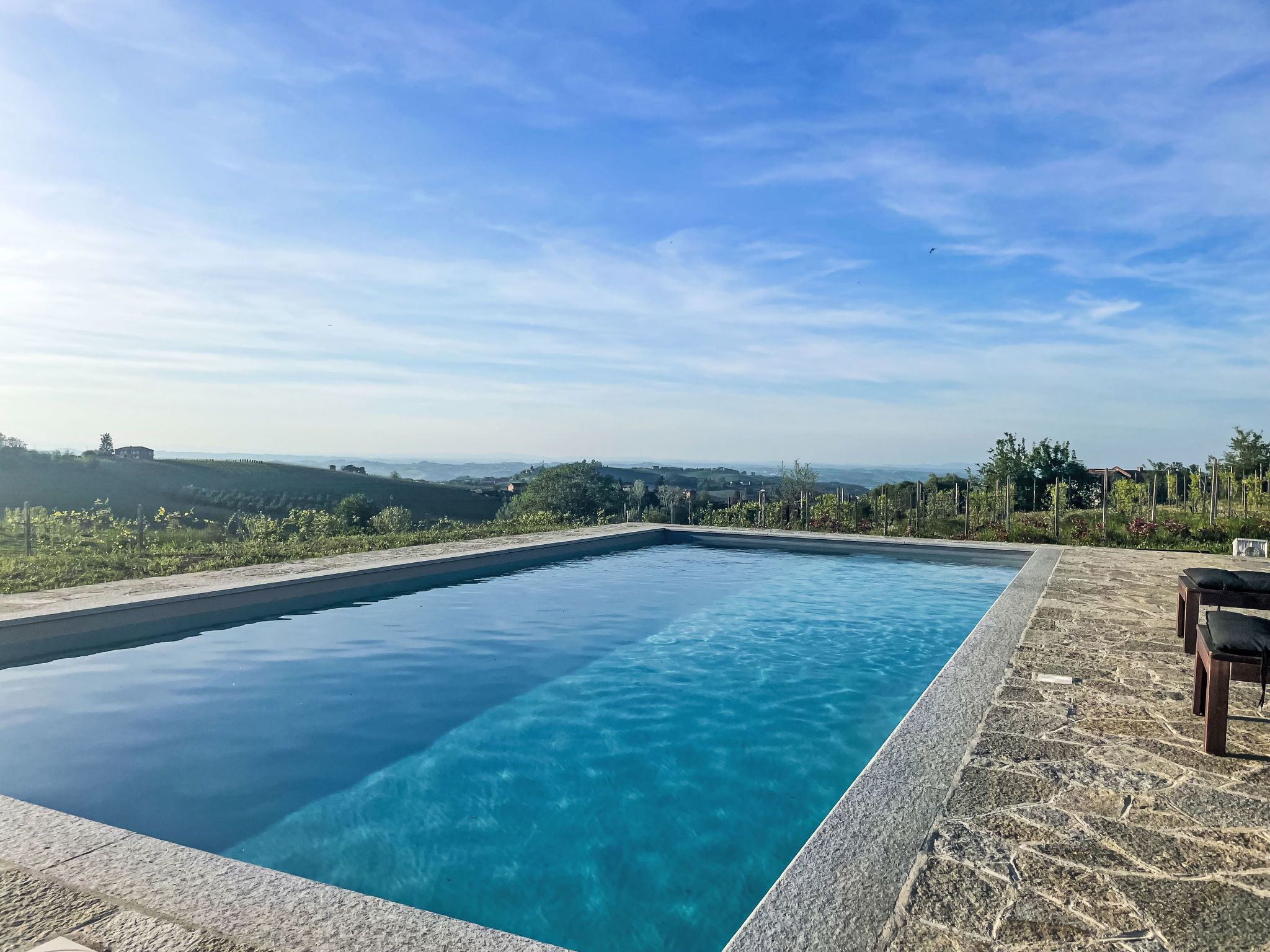 A rectangular infinity pool with clear blue water, surrounded by stone tiles, and a wooden bench on the right.