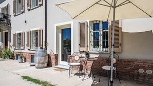 Eine Terrasse im Freien mit Tisch, Stühlen, einem großen Sonnenschirm und einem Fass.