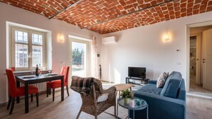 Ein Wohnzimmer mit Ziegeldecke, eine Essecke mit roten Stühlen, ein blaues Sofa und ein Fernseher.