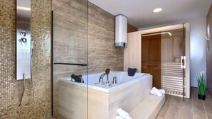 Ein modernes Badezimmer mit einer Glaskabine zur Dusche, einer freistehenden Badewanne und einer Holztür zur Sauna.