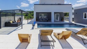 Ein modernes Haus mit Swimmingpool, Sitzgelegenheiten im Freien und einer überdachten Terrasse.