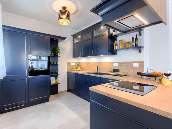 A modern kitchen with dark blue cabinets, a central island, and a built-in oven.