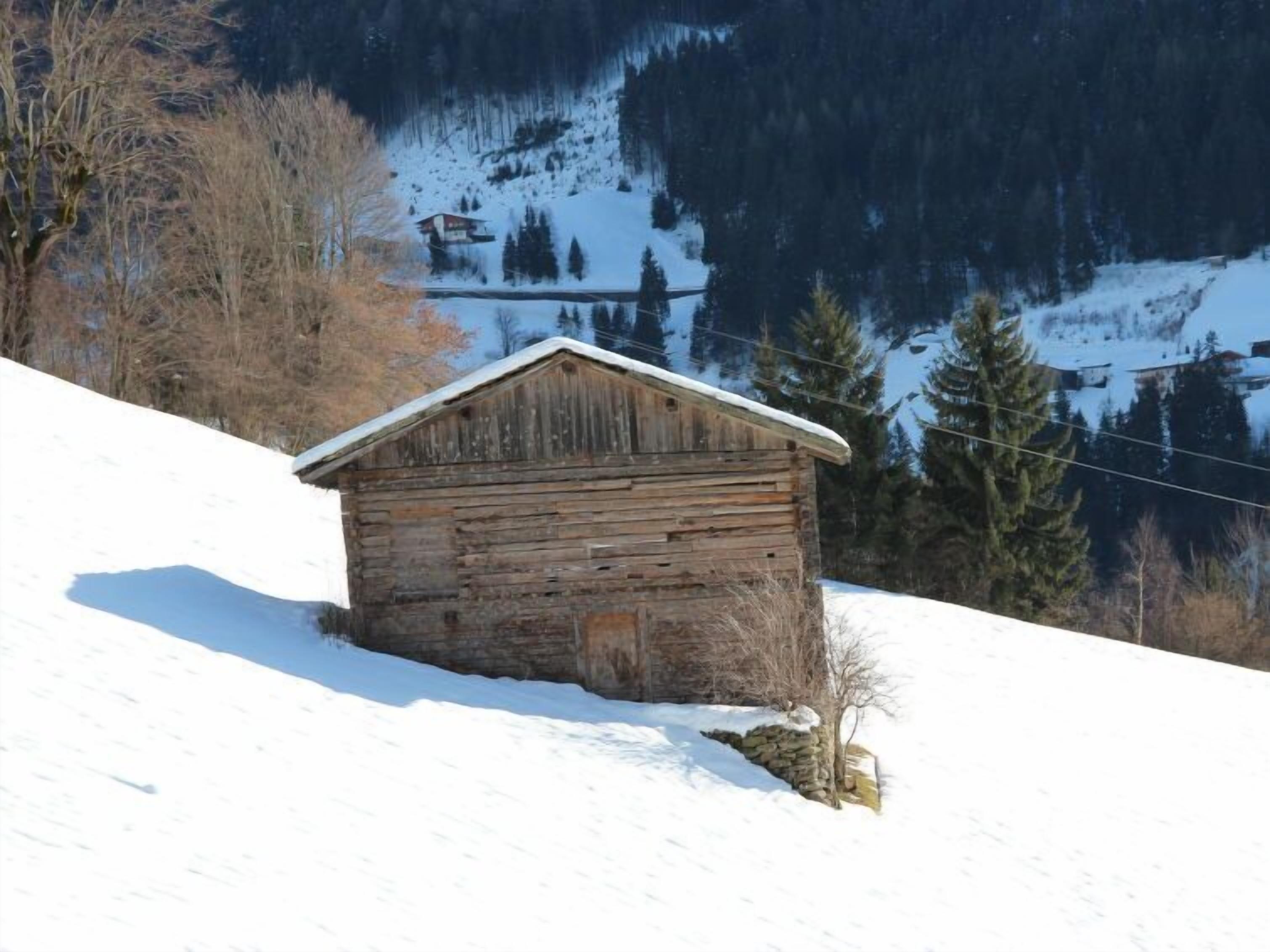 Een houten hut met een schuin dak, omringd door een met sneeuw bedekte grond en bomen.