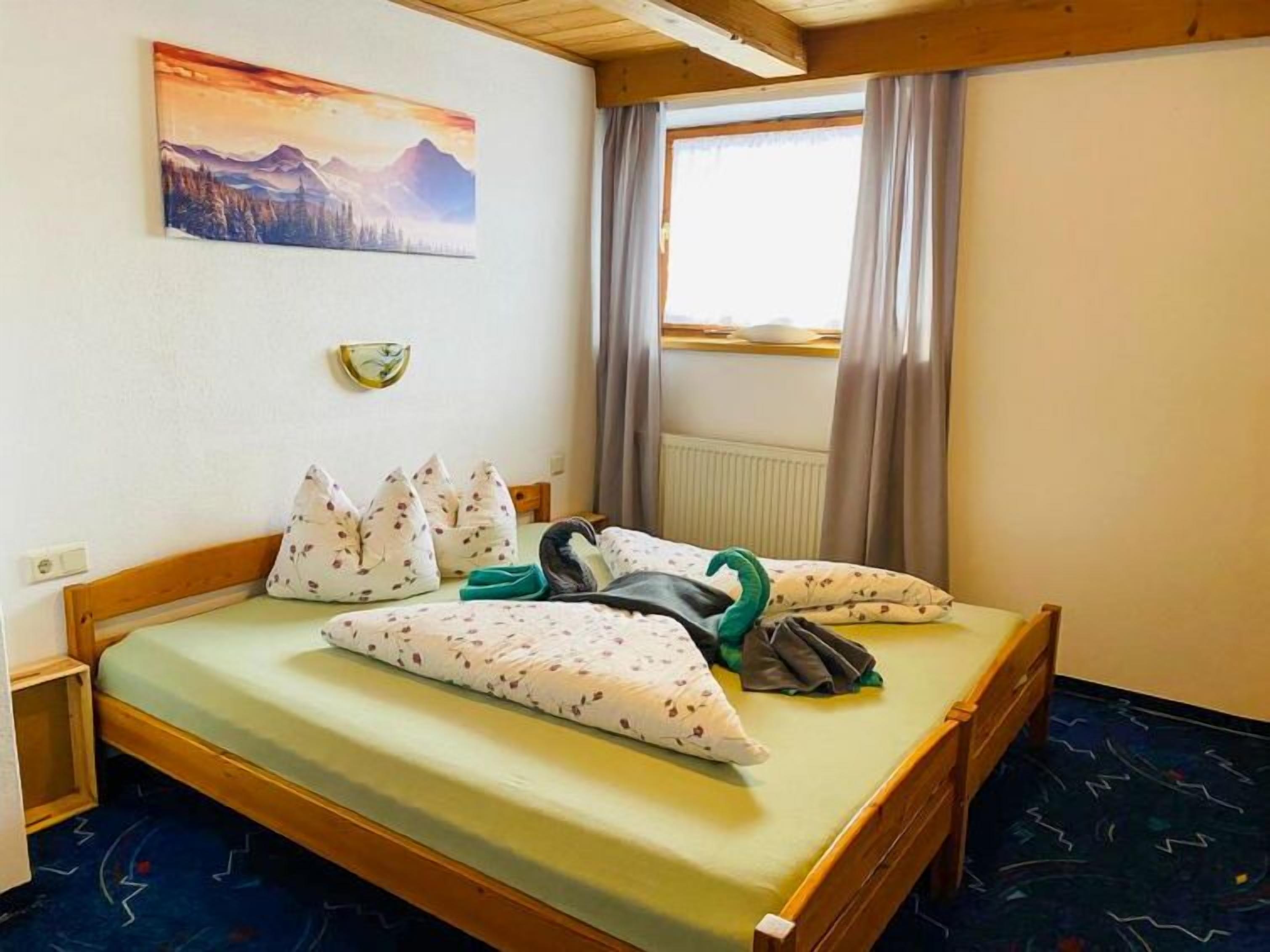 A hotel room with a bed, pillows, a painting, and a window with curtains.