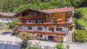 A multi-story wooden chalet with balconies adorned with flowers, a parking area, and a mountainous backdrop. - Gerlosblick by Interhome (Zell am Ziller)