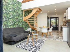 A modern living space with a grey sofa, a glass coffee table, a spiral staircase, and a kitchen area.