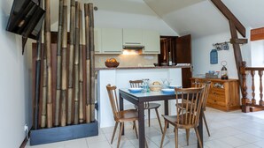 Un coin repas avec une table dressée pour quatre personnes, des chaises en bois et un téléviseur fixé au mur.