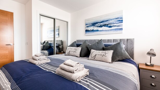 A neatly made bed with a blue and white striped bedspread, grey pillows, and a folded towel on the side. - Jules By The Sea Anstruther (Anstruther)