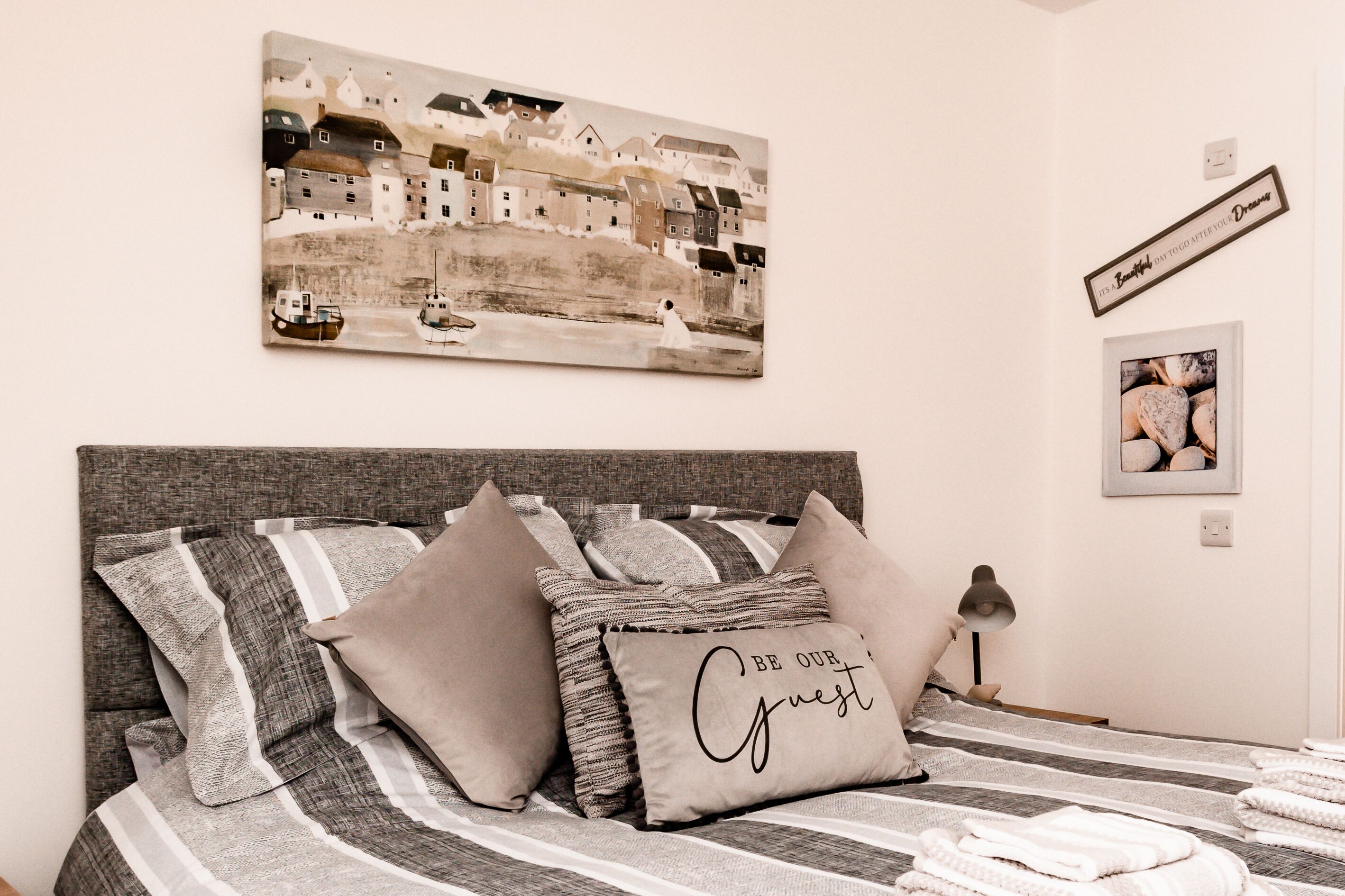 Un dormitorio con cama, almohadas, mesita de noche, lámpara y una obra de arte en la pared.