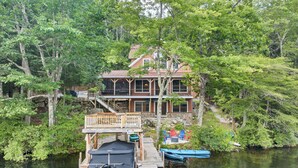 Eine Holzhütte am Seeufer mit Steg, überdachtem Boot und Terrasse mit Außenmöbeln.
