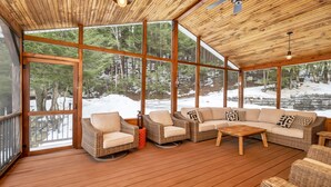 Eine großzügige Holzterrasse mit Korbmöbeln, große Fenster mit Blick auf einen verschneiten Wald.