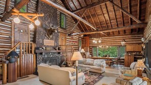 Interior rústico de una cabaña de troncos con chimenea de piedra, mobiliario de madera y una zona de estar acogedora.