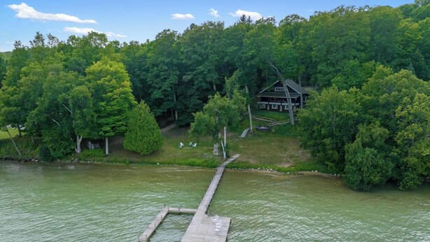Una cabaña junto al lago con un muelle que se adentra en el agua, rodeada de un bosque frondoso.