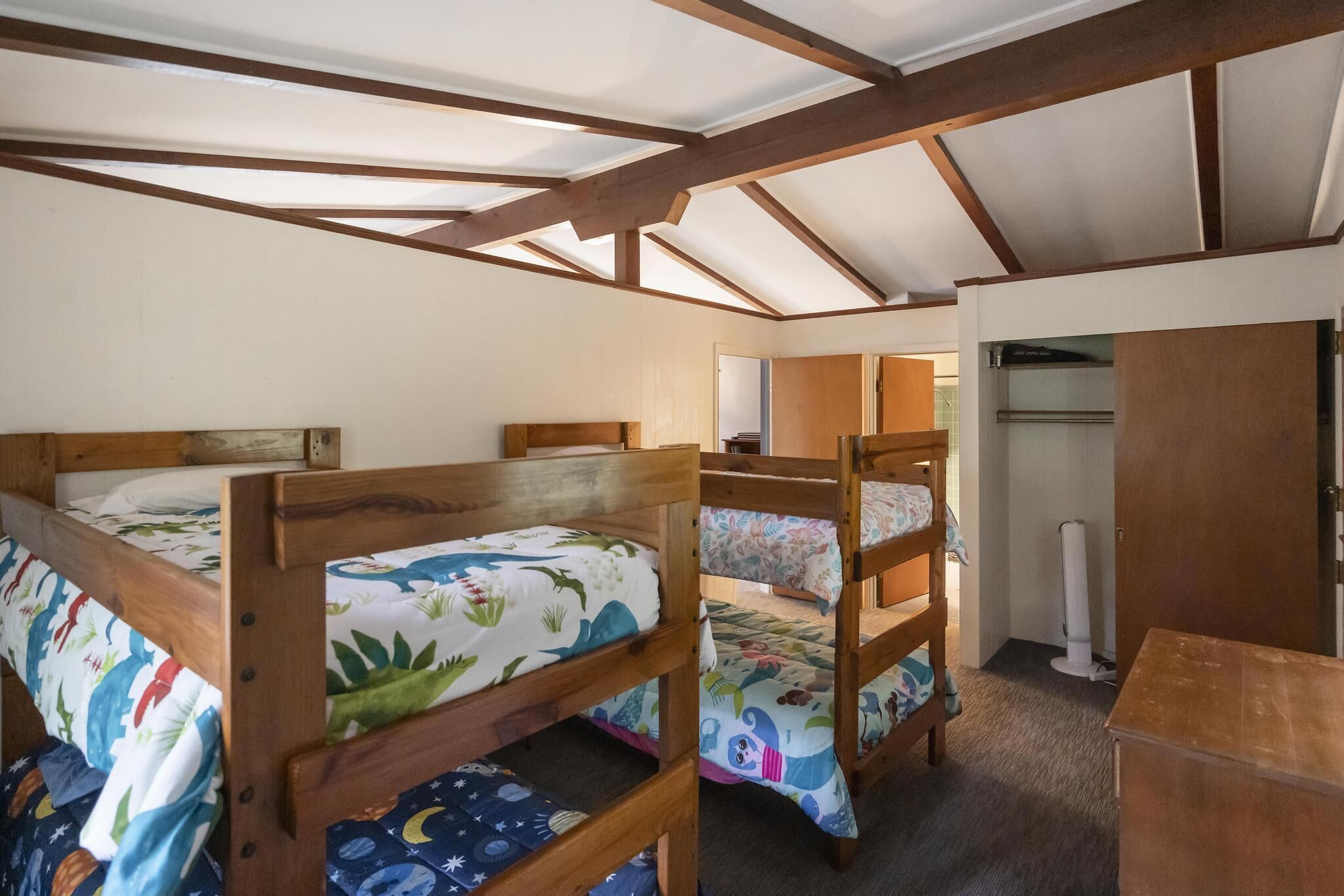 Een slaapzaal met stapelbedden, houten balken en een plafondventilator.