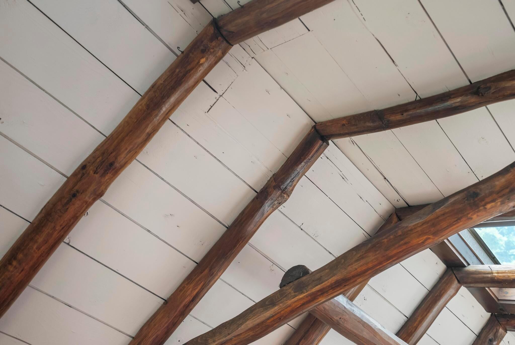 Une structure de plafond en bois avec des poutres apparentes et une lucarne.