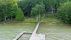 Un muelle de madera se extiende sobre un lago, rodeado de exuberante vegetación y una cabaña al fondo.