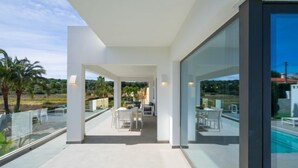 A modern outdoor patio with a glass balustrade, a pool, and a dining area with white furniture. - La Haya by Interhome (Moraira)