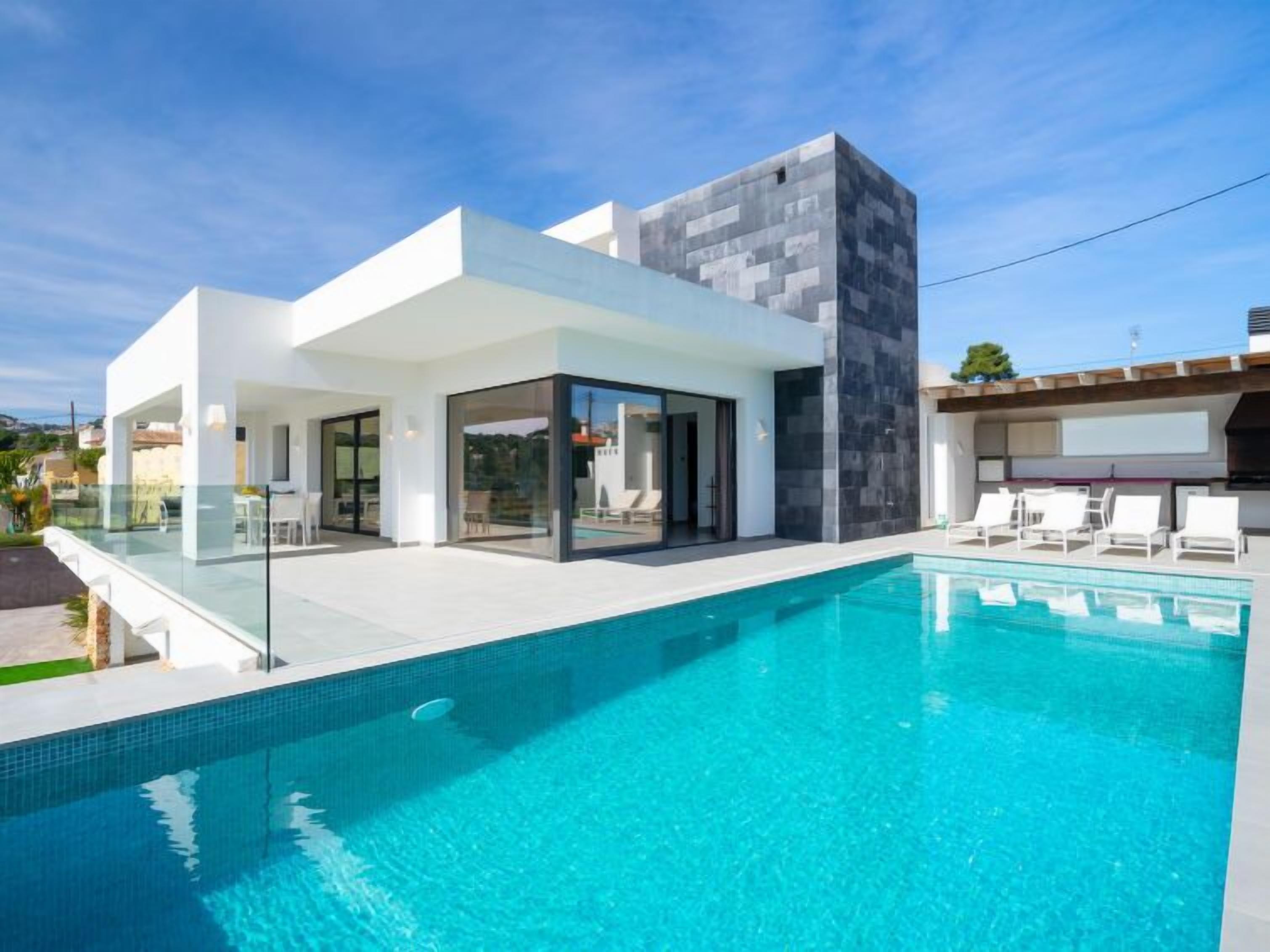 A modern house with a swimming pool, glass doors, and a patio area with lounge chairs.