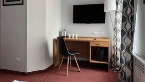 A hotel room with a wooden desk, black chair, a flat-screen TV mounted on the wall, a white lamp, and a patterned curtain. - Garbarska 22 Aparthotel (Kraków)