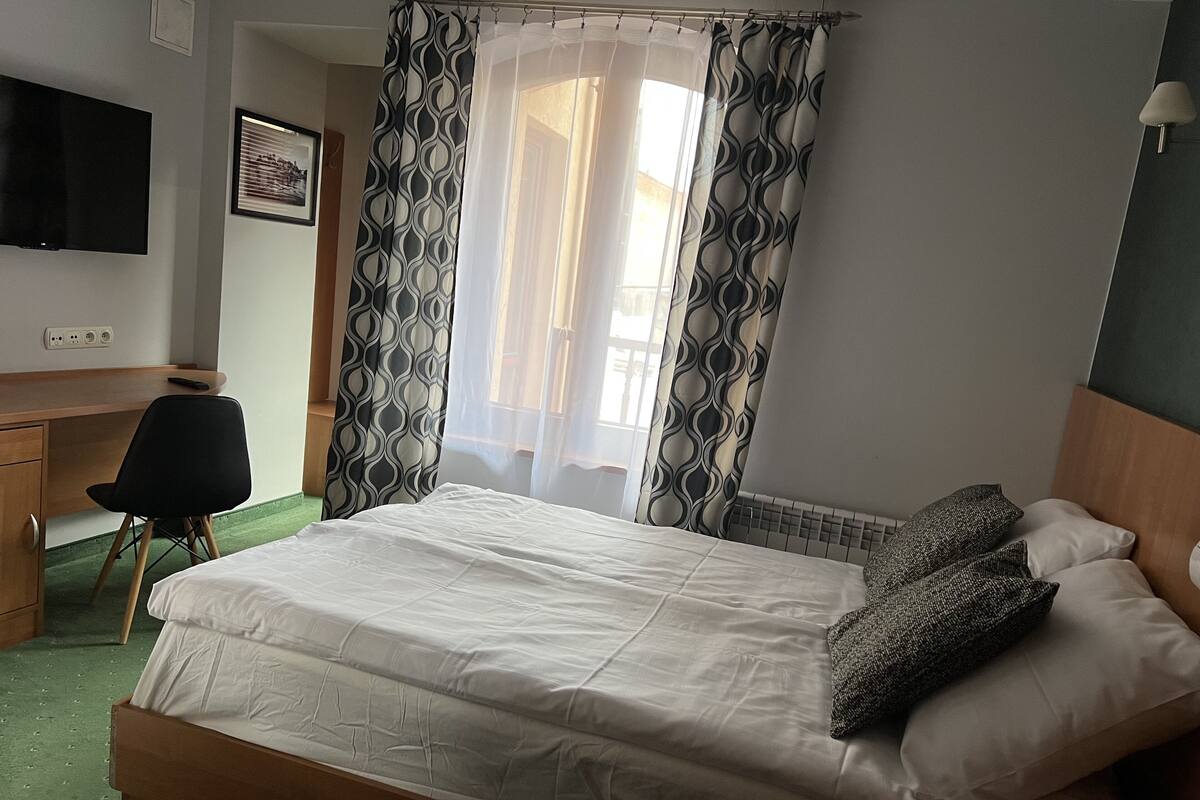 A hotel room with a bed, a desk, a chair, a TV, and a window with curtains.
