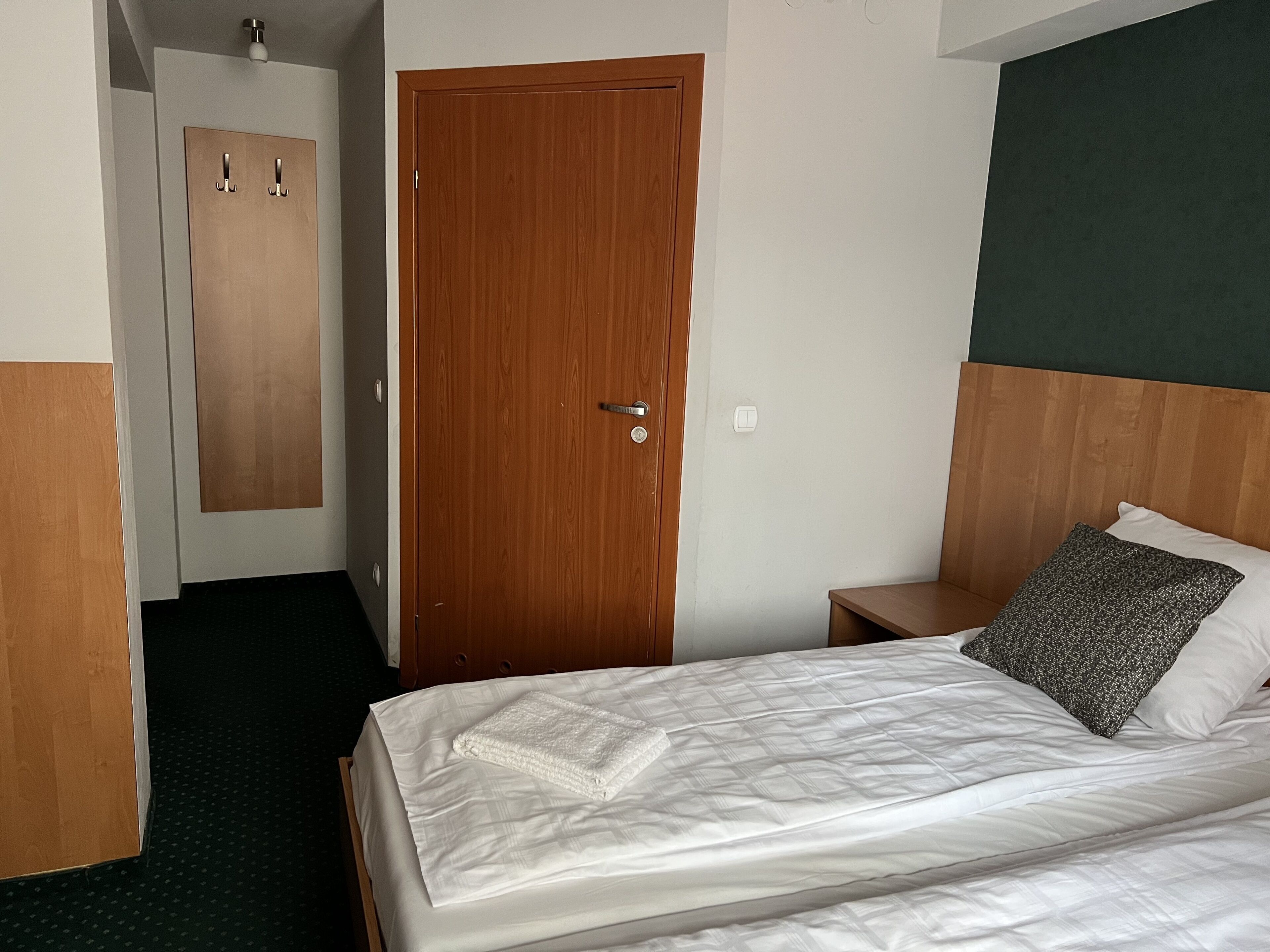 Une chambre d’hôtel avec une porte en bois, un lit avec une literie blanche, une table de chevet et un mur d’accent vert.