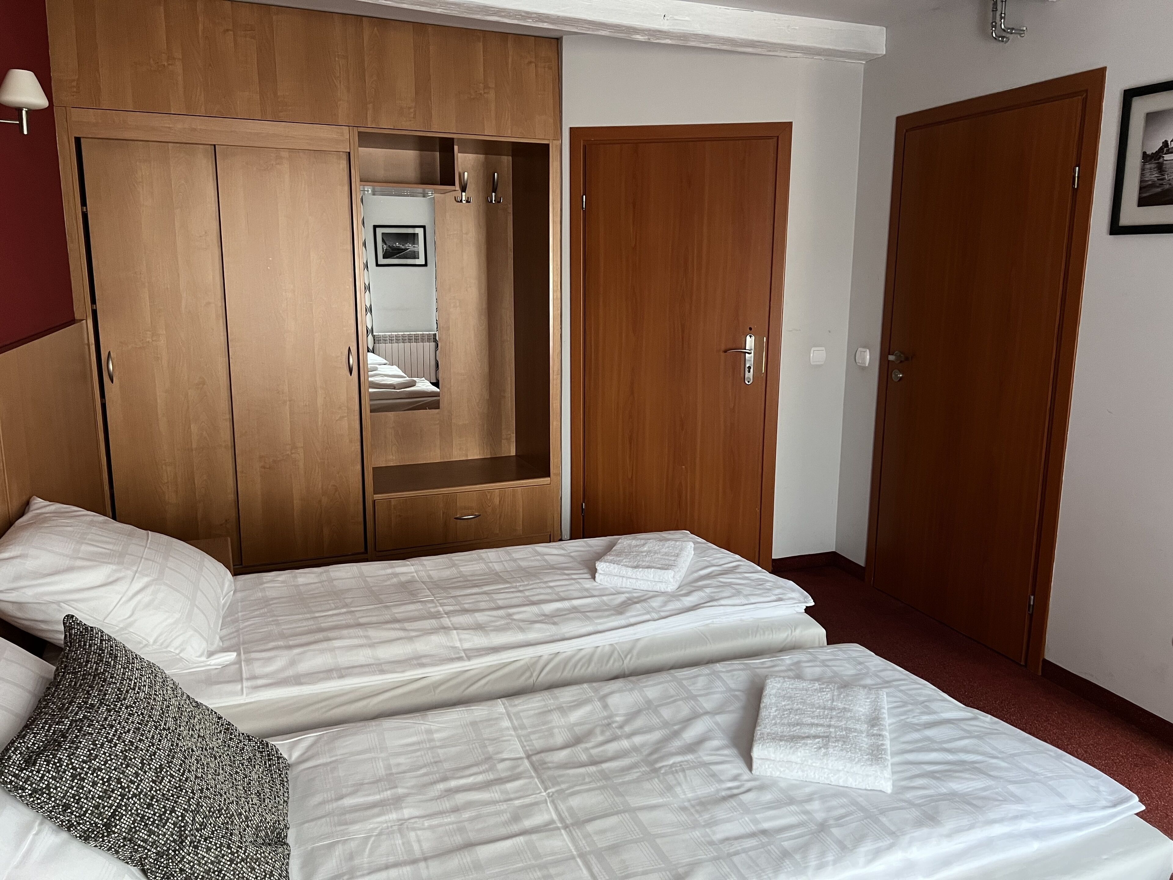Quarto de hotel com duas camas, um guarda-roupa de madeira, um espelho e uma porta.