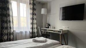 A hotel room with two beds, a desk with a chair, a TV, and a radiator. - Garbarska 22 Aparthotel (Kraków)